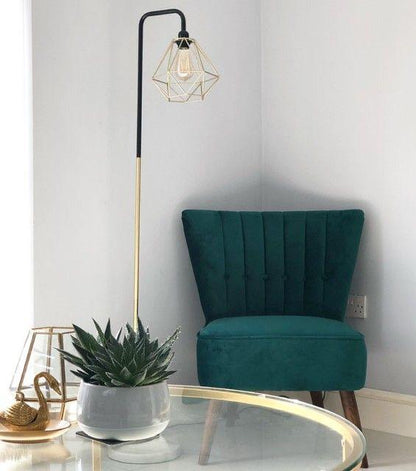 Sillón Matero Virgilio verde petróleo en un rincón, junto a una lámpara de pie y una mesa de vidrio