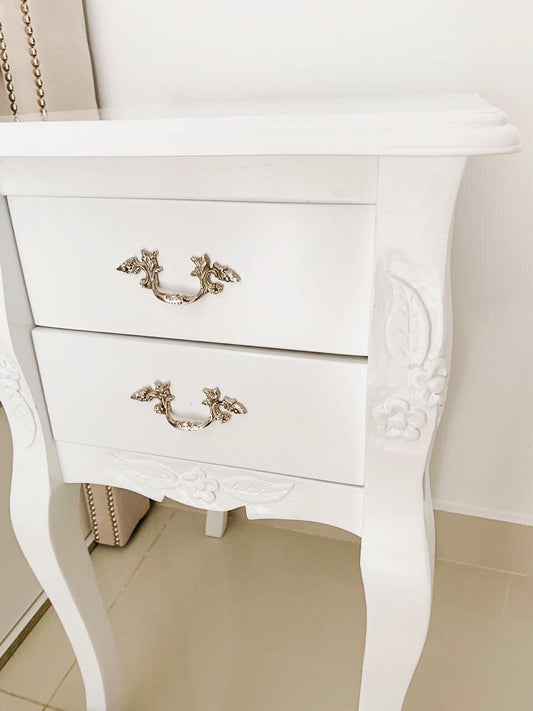 Mesa de Luz Bailarina Gillis laqueada en blanco, con dos cajones, tiradores plateados y tallas de hojas y flores