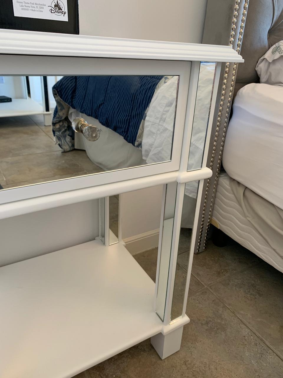 Mesita de luz espejada con cajón y tirador de cristal, junto al Respaldo Emmy gris con tachas