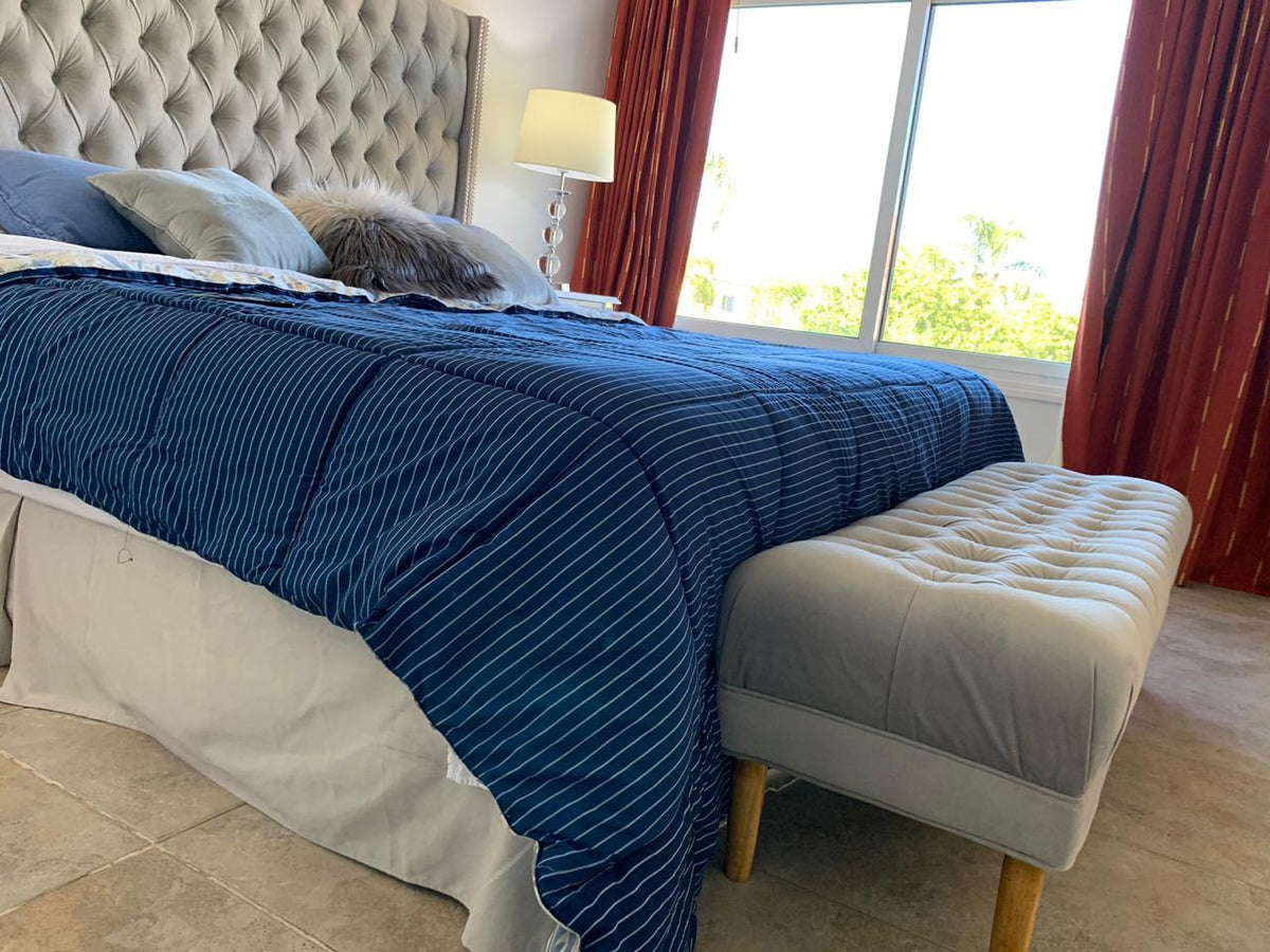 Pie de cama tapizado gris capitoné a los pies de la cama, con cortinas rojas y vista al jardín