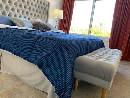 Pie de cama tapizado gris capitoné a los pies de la cama, con cortinas rojas y vista al jardín