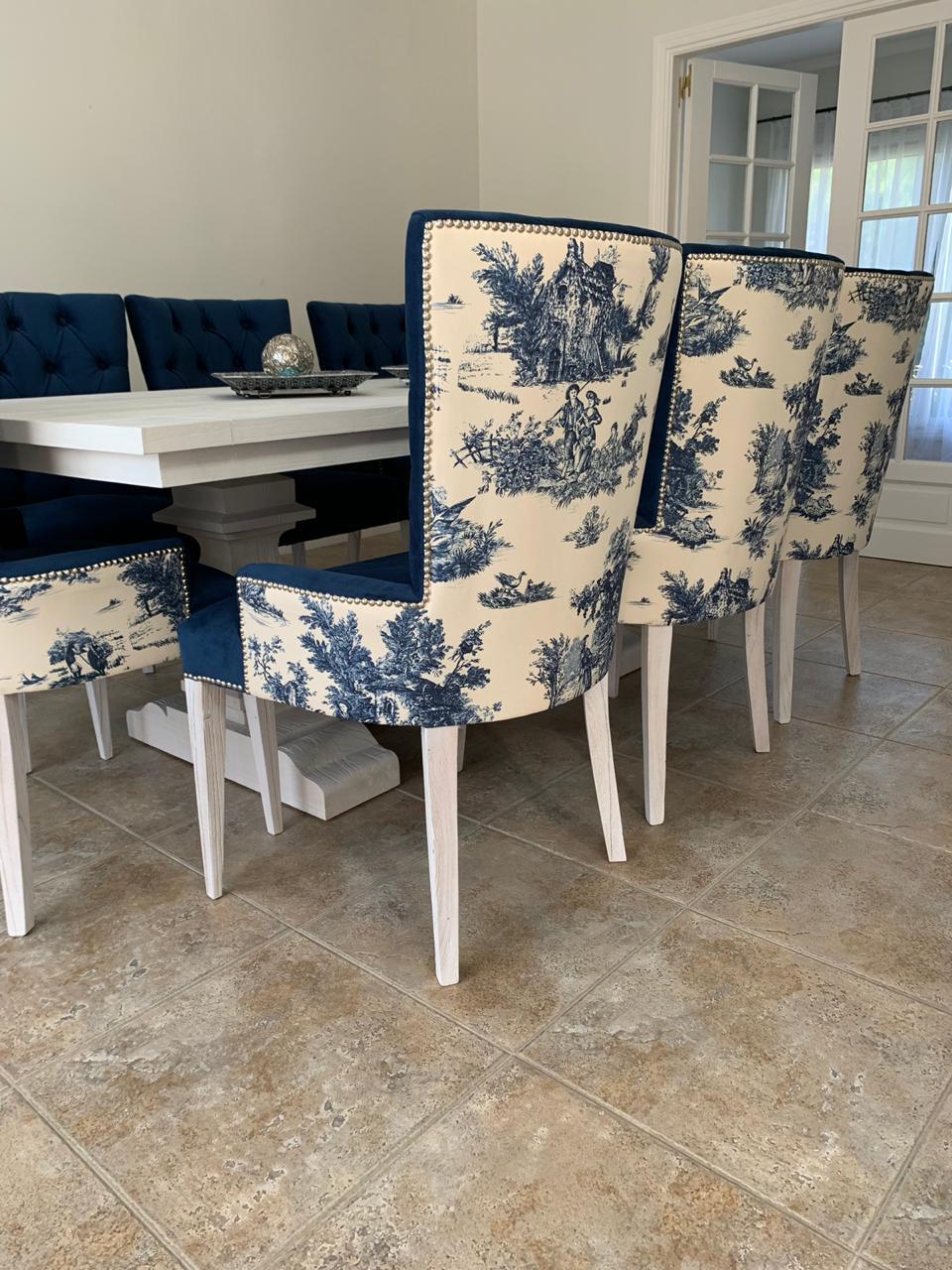 Sillas Menphis tapizadas en estampado toile azul y blanco, con tachas plateadas y patas blancas, junto a sillas de terciopelo azul capitoné