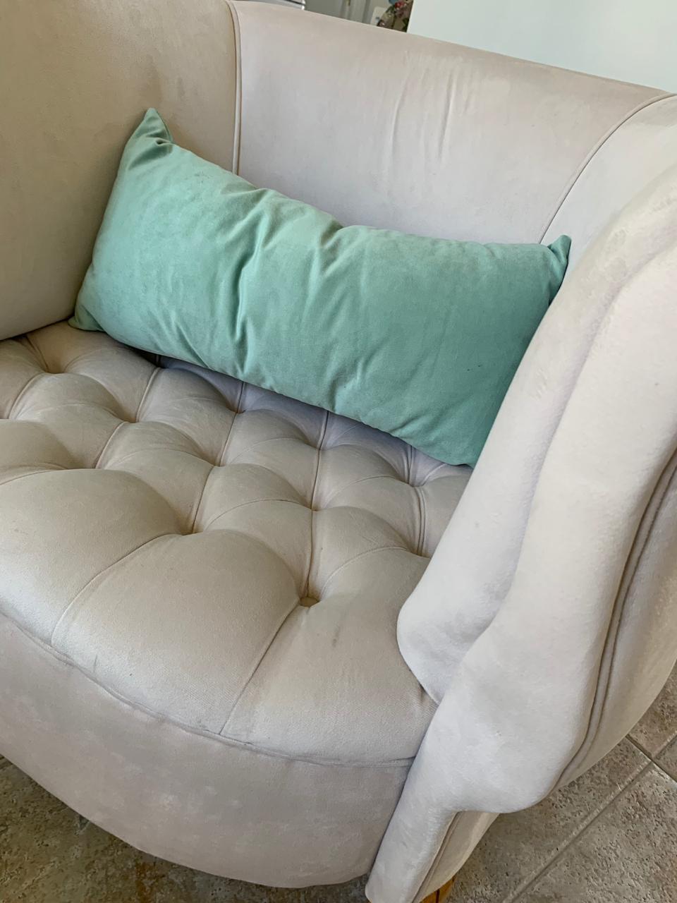 Detalle del asiento capitoné del Sillón Brigitte en beige claro, con almohadón verde agua y manta
