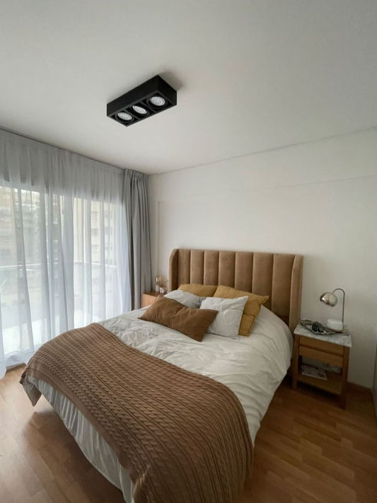 Respaldo Alpes camel con canales verticales y orejas, en el dormitorio en tonos tierra de Julieta, junto al ventanal