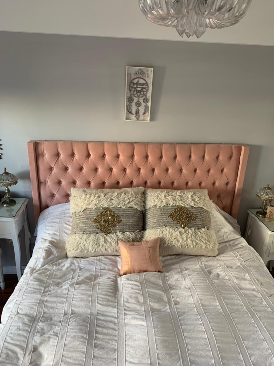 Vista frontal del Respaldo Emmy rosa de Camila, con almohadones crudos y lámpara de cristal
