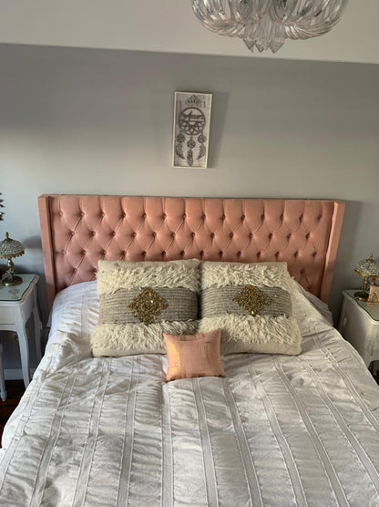 Vista frontal del Respaldo Emmy rosa de Camila, con almohadones crudos y lámpara de cristal