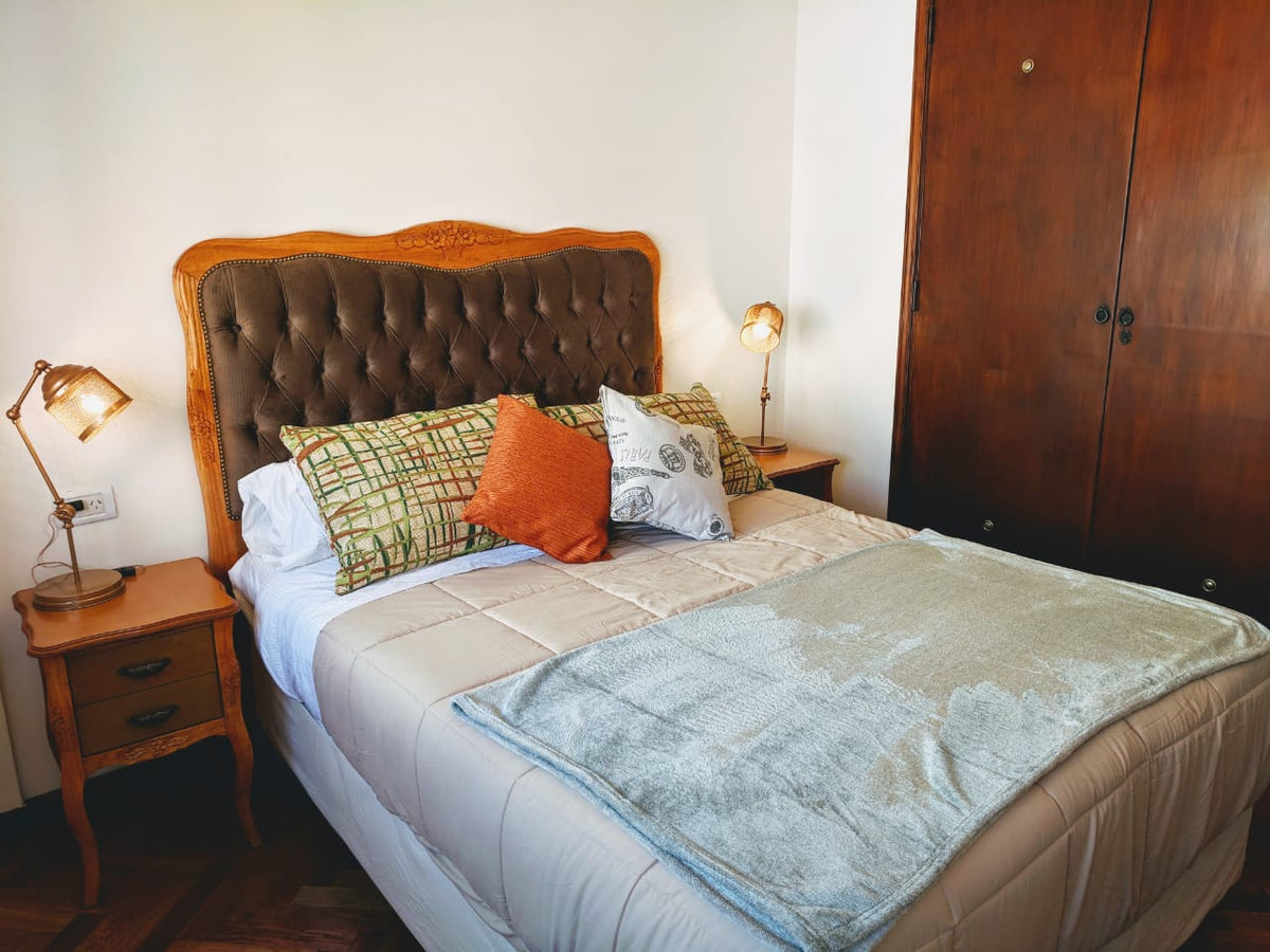 Vista del dormitorio de Estela con el respaldo retapizado en capitoné marrón y una Mesa de Luz Bailarina junto al placard