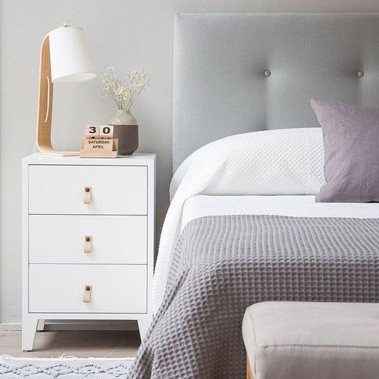 Respaldo de Cama Botón gris con botones forrados, junto a una mesa de luz blanca y una lámpara de madera