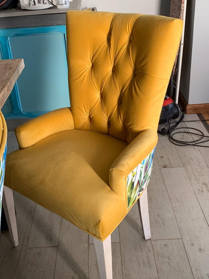 Silla Menphis en terciopelo amarillo con capitoné, apoyabrazos y patas blancas, en el comedor de Gabriela