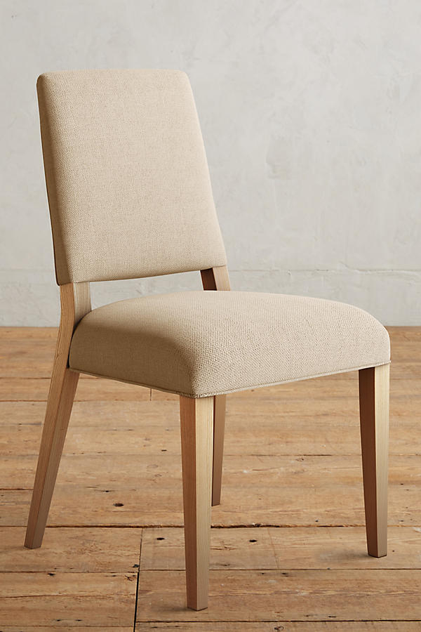 Silla Nude tapizada en crema, con patas de madera, sobre piso de madera