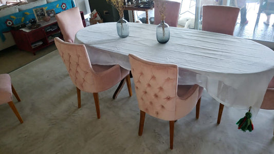 Sillas Charis con respaldo capitoné en pana Velutti color Apricot y patas de madera, alrededor de la mesa ovalada del comedor de Sonia