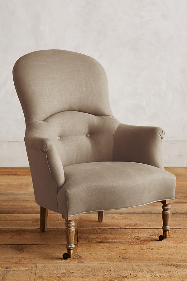 Sillón individual de diseño tradicional en tono beige, con respaldo curvo, apoyabrazos tallados y patas delanteras de madera con ruedas.