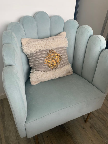 Sillón Angie tapizado en celeste, con respaldo de líneas curvas y un almohadón de textura en tonos neutros, en el living de Delfina