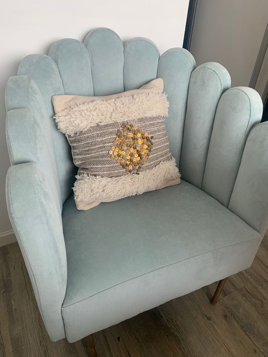Sillón Angie tapizado en celeste, con respaldo de líneas curvas y un almohadón de textura en tonos neutros, en el living de Delfina