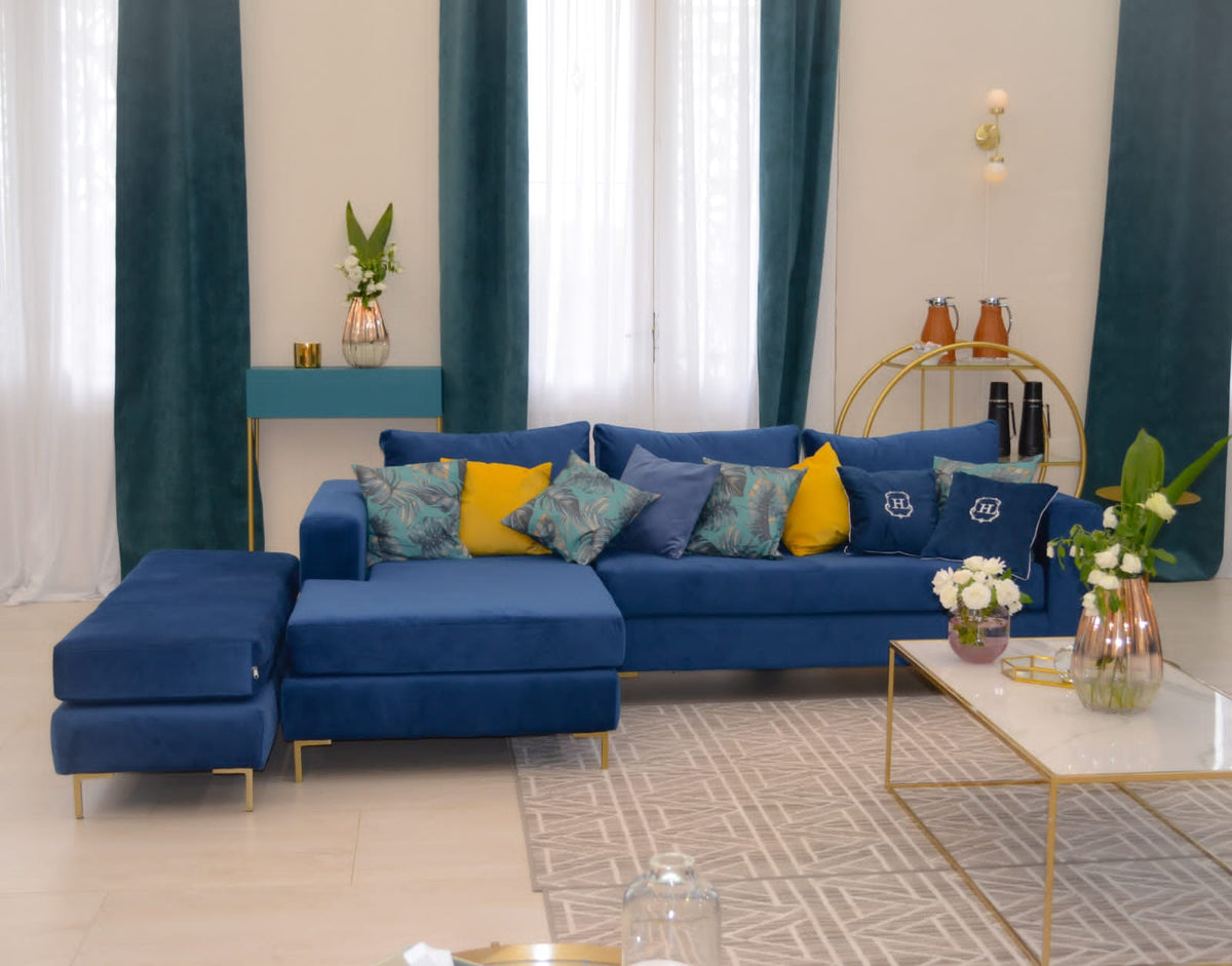 Sillón esquinero Magnolia en azul visto de frente, con mesa ratona dorada y almohadones amarillos
