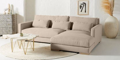 Sillón esquinero Steven en beige con mesas ratonas doradas, en un living con jarrón de pampas