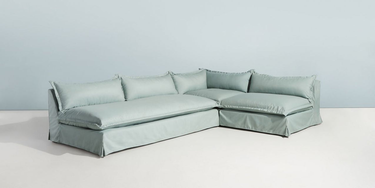 Sillón esquinero Tassa enfundado en gris claro, vista en diagonal del respaldo alto y los almohadones sueltos