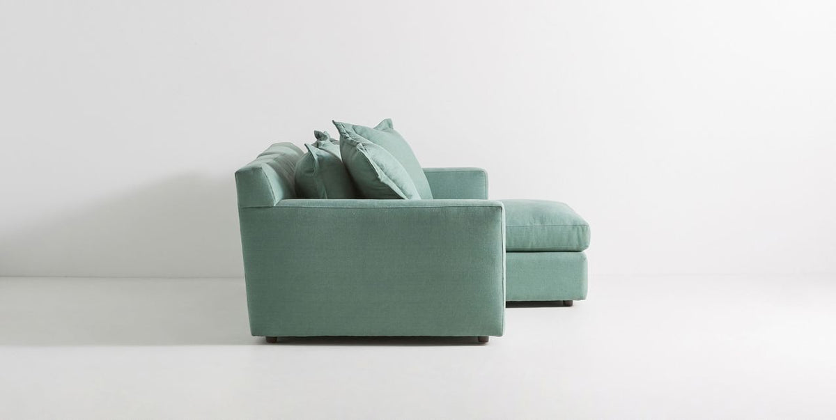 Sillón esquinero Enrique en verde claro visto de frente, con planta y mesa auxiliar de ratán