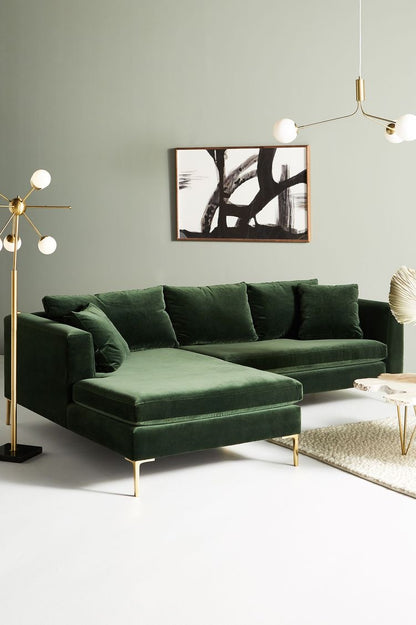 Sillón esquinero Magnolia en pana antimanchas verde inglés con patas doradas, en un living con cuadro y lámpara de pie