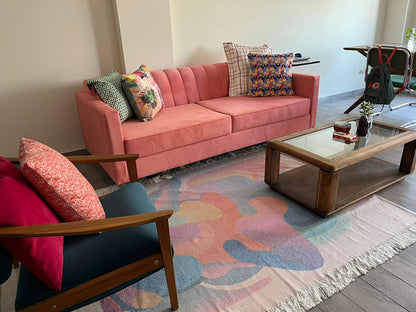 Sillón de dos plazas tapizado en terciopelo rosa, con diseño moderno de líneas rectas y estructura firme. Su color vibrante aporta un toque de personalidad al espacio, mientras que los cojines decorativos en tonos variados refuerzan un estilo acogedor y contemporáneo. Ideal para salas con carácter y decoración ecléctica.