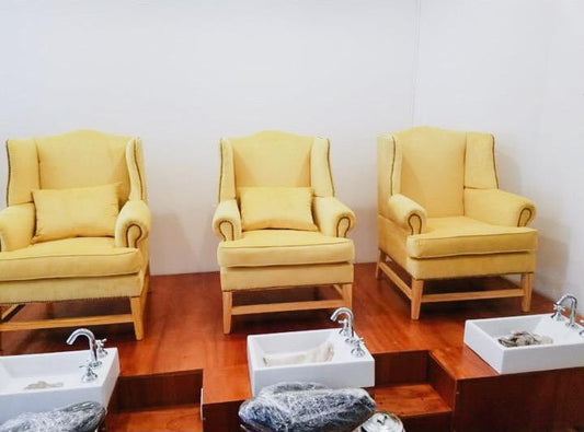 Tres Sillones Flower amarillos, tipo bergère con tachas y patas de madera cruzadas, usados como sillones de pedicura en el spa de Sofía en Santa Fe
