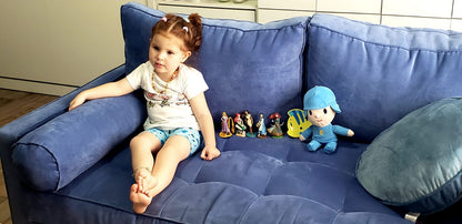 Hija de Romina sentada en el Sofá Bambú azul, con almohadones cilíndricos en los brazos y asiento botoné