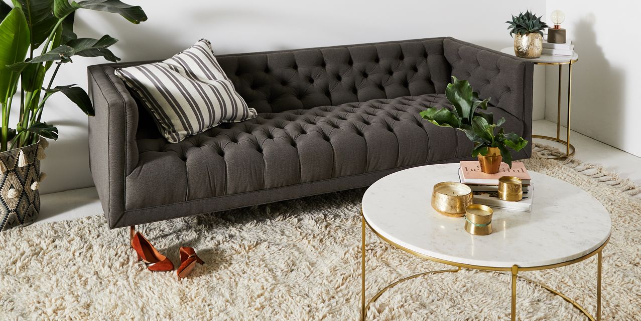 Sofá Bella Donna Capitoné tapizado en gris, ambientado en living con planta y mesa ratona - Tienda de Banquitos