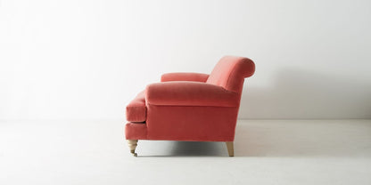 Sofá Cecily tapizado en velvet coral, vista lateral mostrando el brazo redondeado y las patas torneadas con rueditas - Tienda de Banquitos