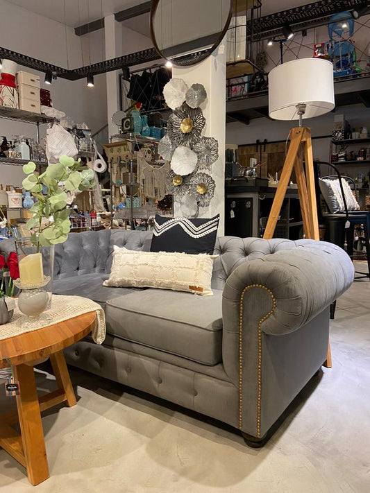 Sofá Chesterfield gris con capitoné y tachas, junto a una mesa de madera, en Hogar & Garden, Córdoba