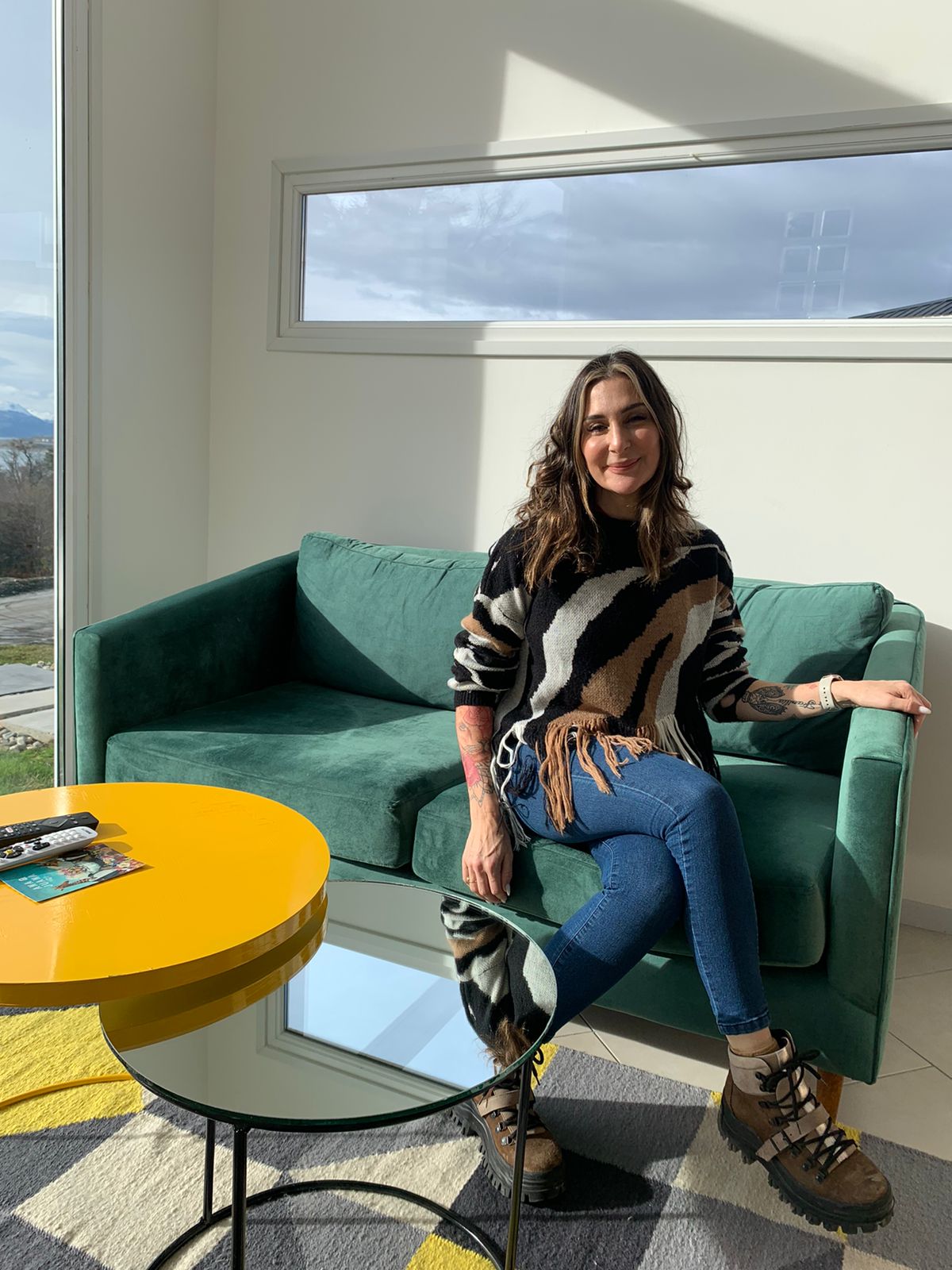 Una mujer sentada en el Sofá Corina verde del loft en Ushuaia, junto a la mesa ratona amarilla
