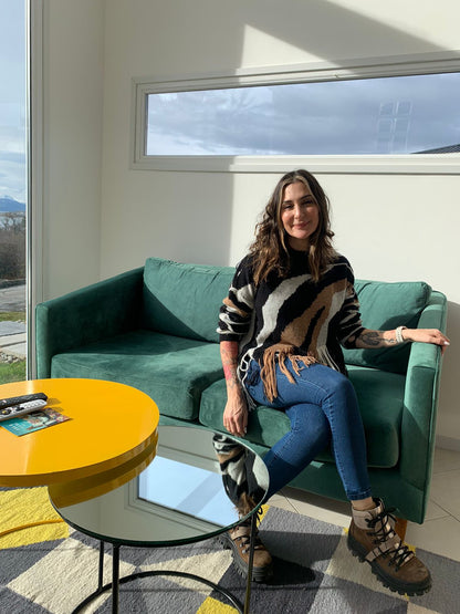 Una mujer sentada en el Sofá Corina verde del loft en Ushuaia, junto a la mesa ratona amarilla