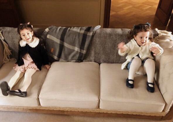 Dos nenas sentadas sobre los tres almohadones del Sofá Deconstructed beige, con la base de madera a la vista