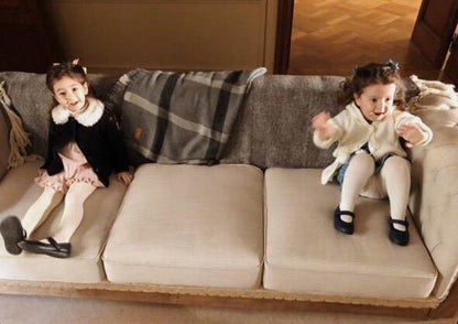 Dos nenas sentadas sobre los tres almohadones del Sofá Deconstructed beige, con la base de madera a la vista