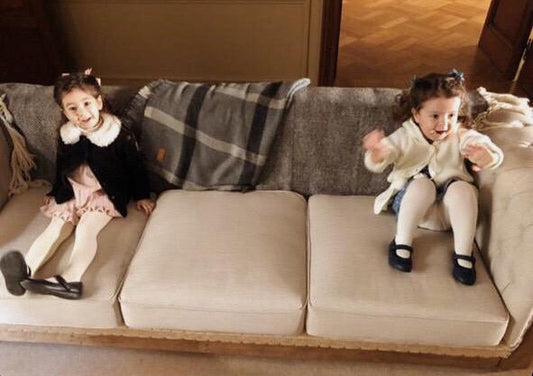 Dos nenas sentadas sobre los tres almohadones del Sofá Deconstructed beige, con la base de madera a la vista