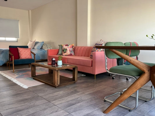 Living comedor de Mari con el Sofá Mila coral al fondo, mesa ratona de madera y sillas verdes en primer plano