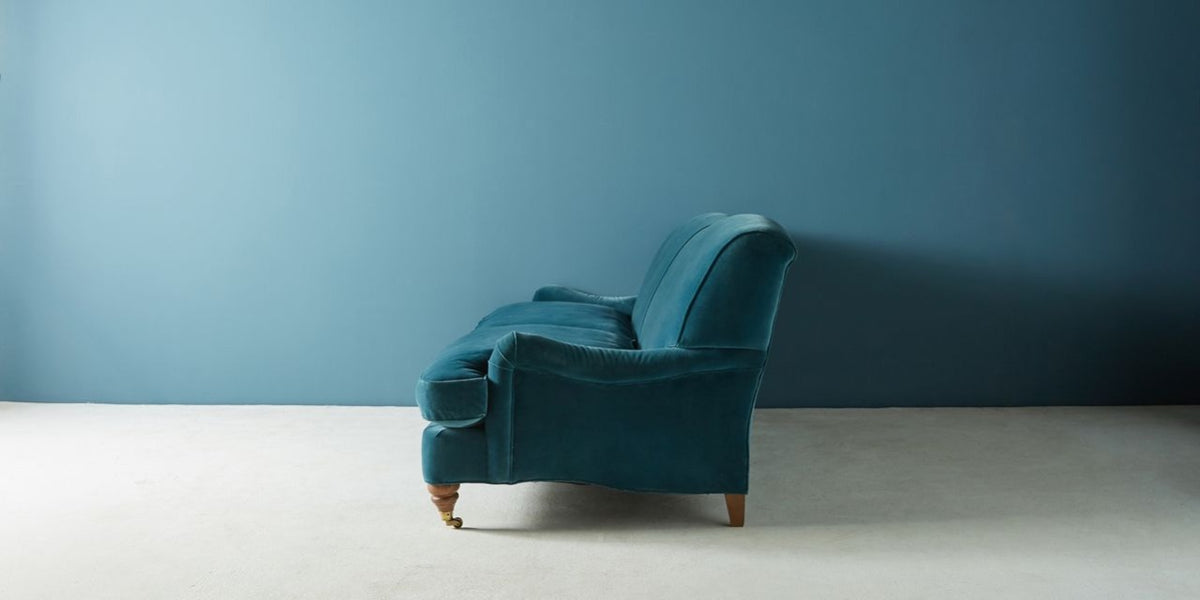 Sofá Minerva color azul petróleo, vista lateral del brazo bajo enrollado y patas torneadas - Tienda de Banquitos